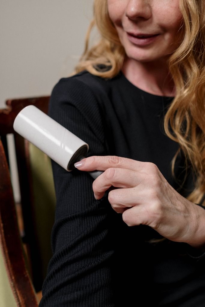 Close-up of a woman using a lint roller to clean her black sweater indoors.